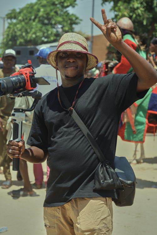 Free Smiling photographer with camera gear at a lively outdoor event. Stock Photo