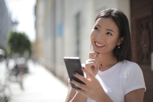 Free A happy woman with a smartphone, enjoying a sunny day outdoors. Stock Photo