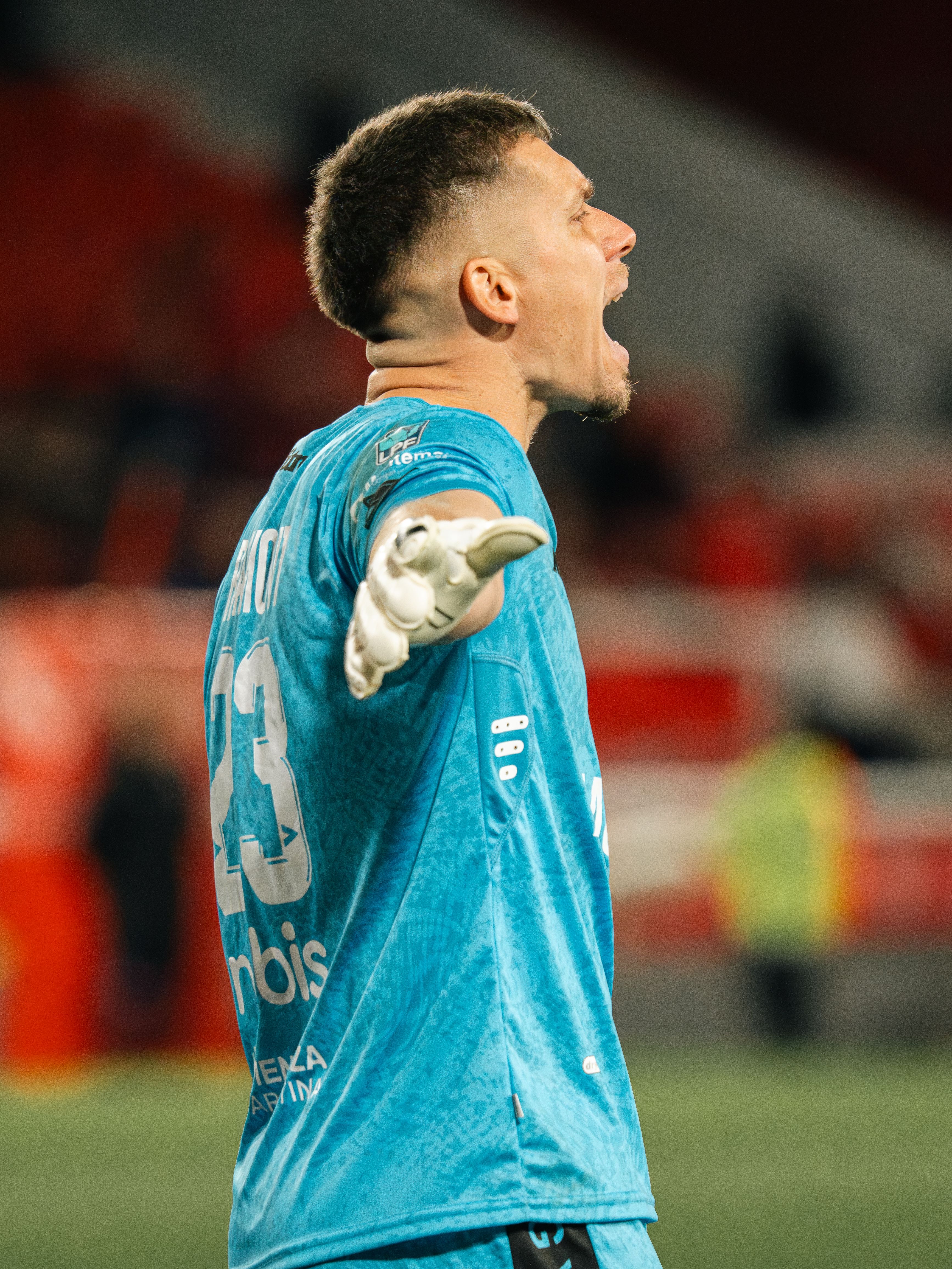 A passionate soccer goalkeeper in blue jersey celebrates a successful save during a match.