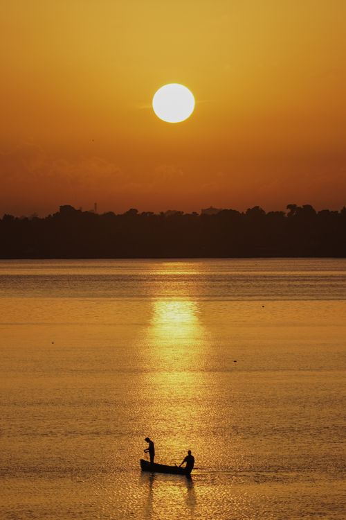 Free Tranquil sunset scene with silhouettes of a boat and fishermen on a serene lake in India. Stock Photo