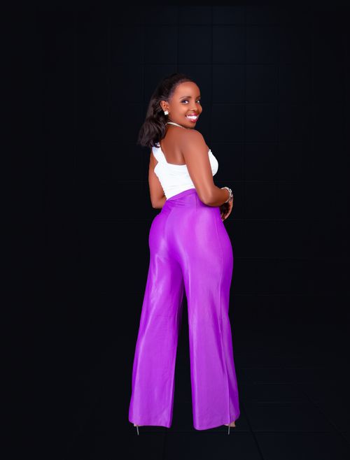 Free Stylish young woman in vibrant purple pants and white top posing indoors with a confident smile. Stock Photo