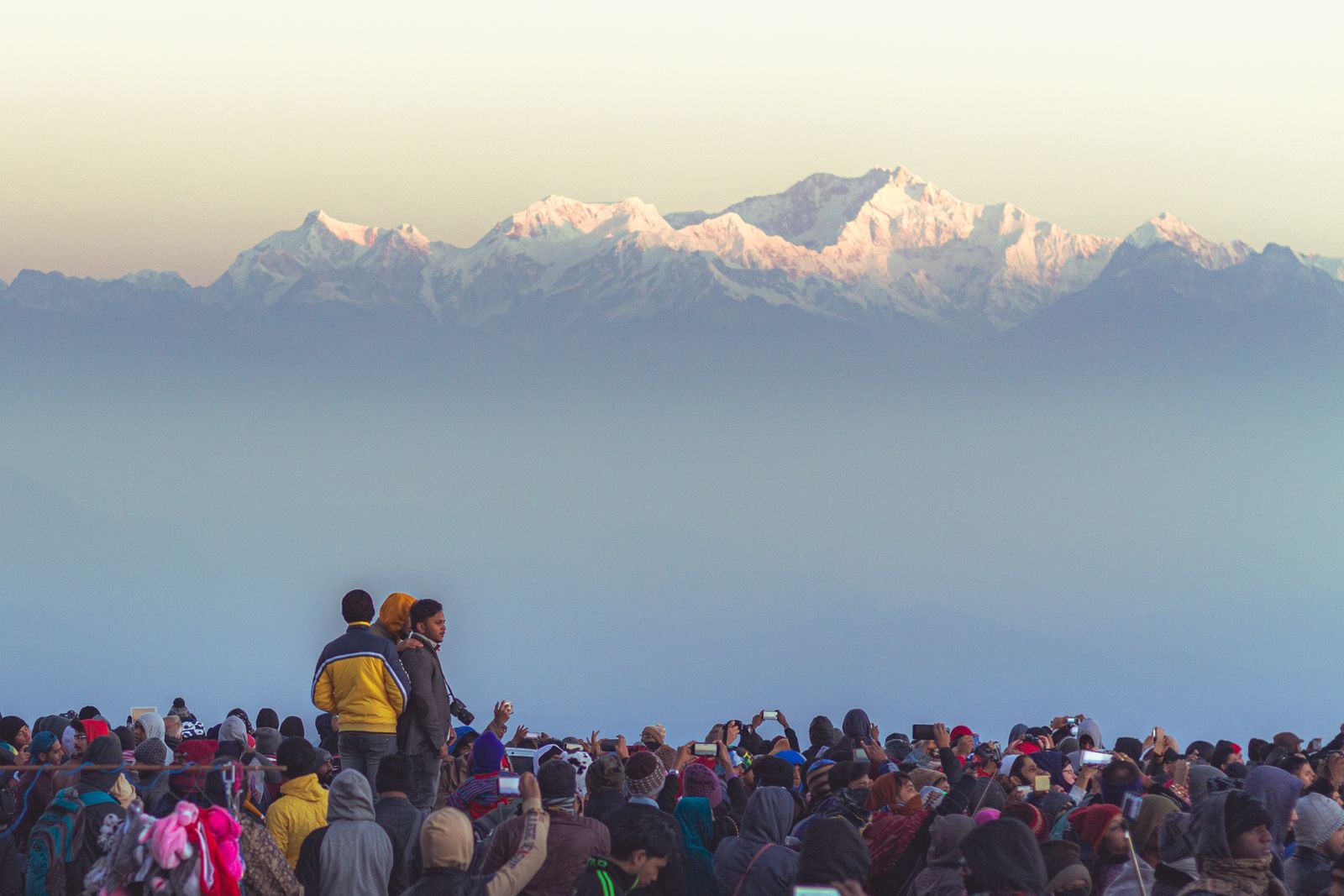 Visitors in coats and woollen hats at dawn watching the Kanchenjunga range turn pink above the haze