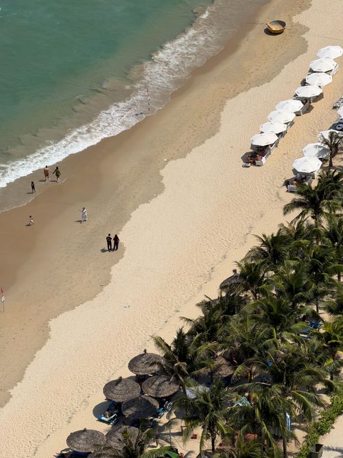Free Aerial view of a beautiful sandy beach in Da Nang, Vietnam, with umbrellas and palm trees lining the shore. Stock Photo