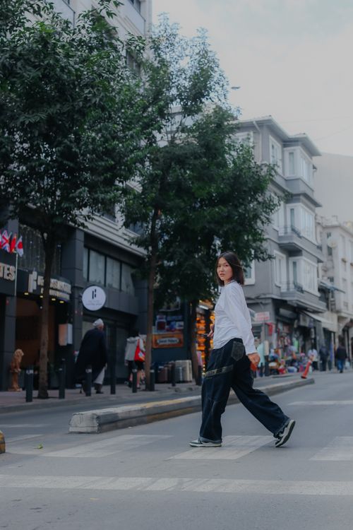 Free A woman confidently crosses a city street, showcasing urban fashion and lifestyle. Stock Photo