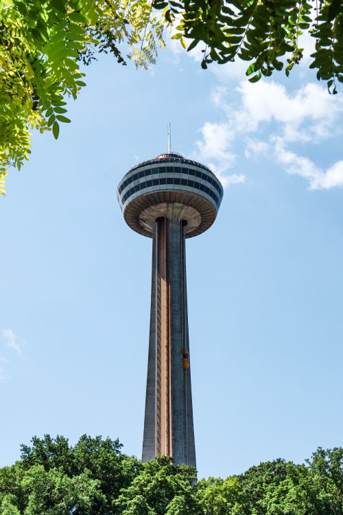 Free View of the Skylon Tower in Niagara Falls, Canada, surrounded by greenery under a clear blue sky. Stock Photo