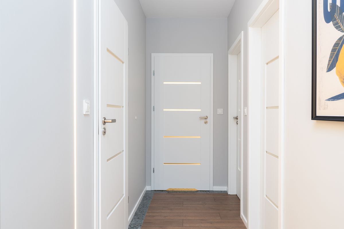 Closed white bedroom doors along a bright hallway with a wooden floor, showing the narrow gap under each door