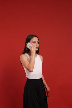 Elegant woman talking on the phone against a bold red backdrop, showcasing modern lifestyle.
