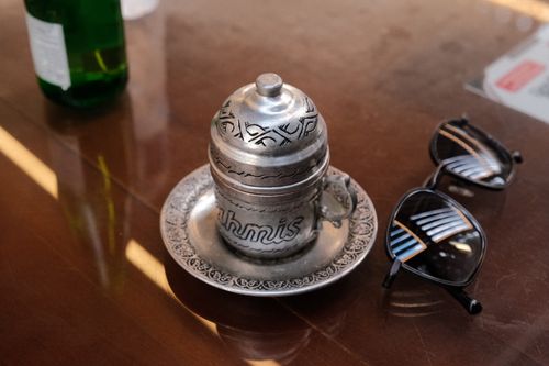 Free An ornate metal cup and saucer with sunglasses on a wooden table. Stock Photo