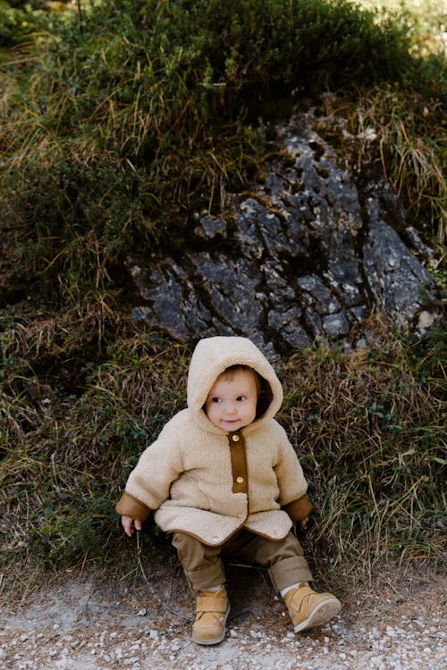 Child in Brown Hoodie Sitting on Green Grass Field