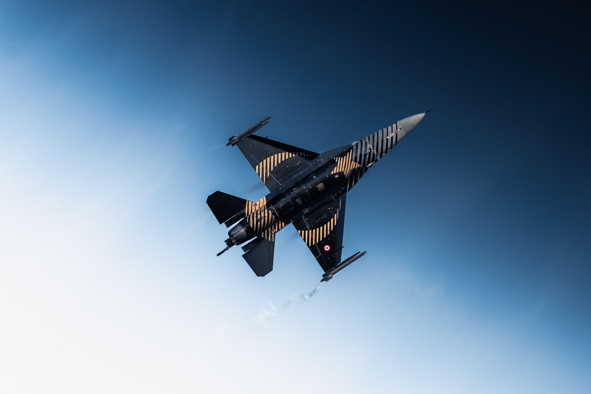 A sleek fighter jet performs an aerial maneuver against a clear blue sky.