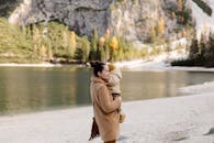 一位母亲在宁静的山湖边拥抱她的孩子，在户外展现温馨的家庭时光