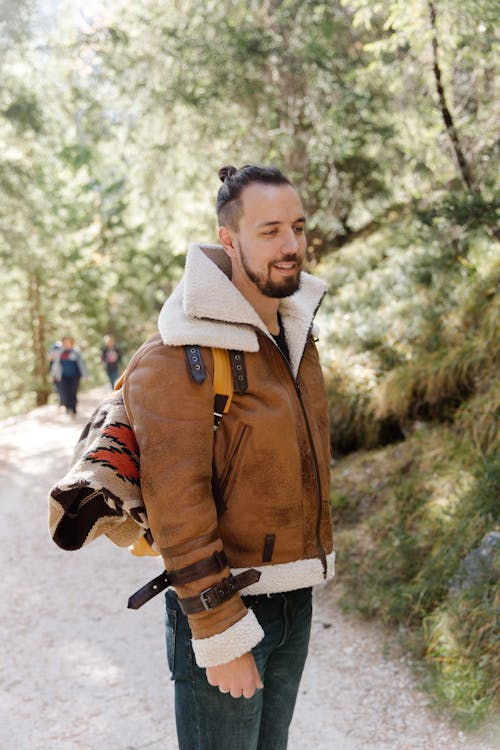 Man in Brown Leather Jacket Standing Near Green Trees