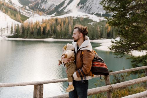 Free Father and child enjoying a winter view by the lake with snowy mountains and trees in the background. Stock Photo