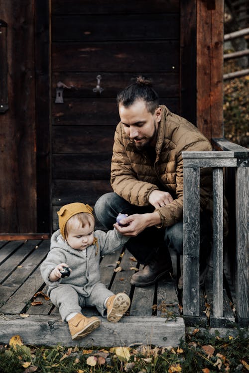 Man in Brown Jacket and Blue Denim Jeans Sitting  Holding His Child