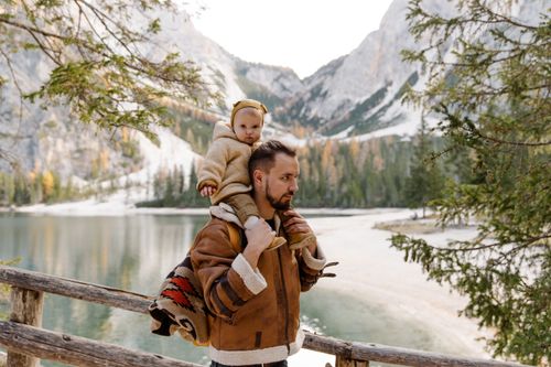 Free Father carrying his child by a serene lake amidst majestic mountains, enjoying nature. Stock Photo