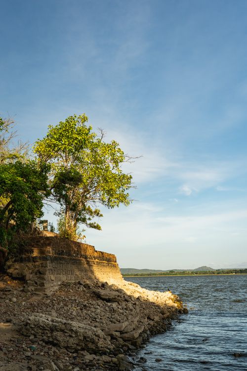 Free A serene lakeside landscape in Polonnaruwa, Sri Lanka featuring rocky shoreline and trees under a clear sky. Stock Photo