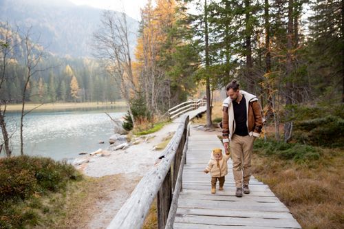 Free Father and child enjoying a walk on a scenic wooden pathway by the lake in autumn. Stock Photo