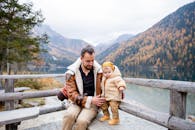 父子俩在湖边欣赏秋日宁静的景色，四周环绕着五彩斑斓的树叶