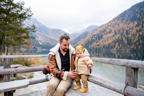 Free A father and child enjoy serene autumn views by a lake, surrounded by colorful foliage. Stock Photo