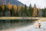 一个年轻的孩子在风景秀丽的湖边，穿着温暖的衣物，欣赏着秋天的山景