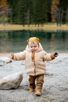 一个可爱的蹒跚学步的孩子穿着温暖的夹克，走在秋天宁静的沙质湖岸上