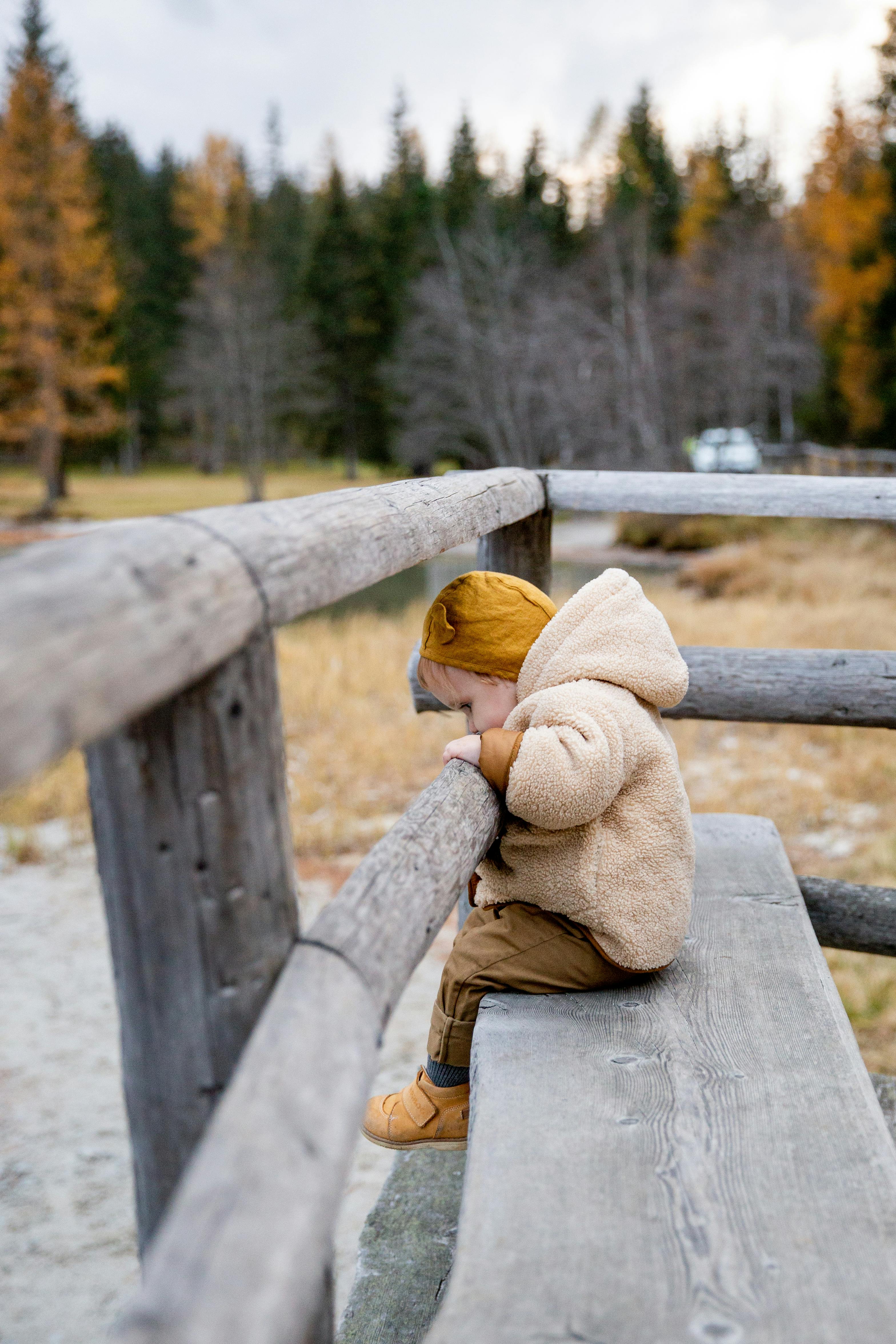 photo of baby leaning on wooden fence