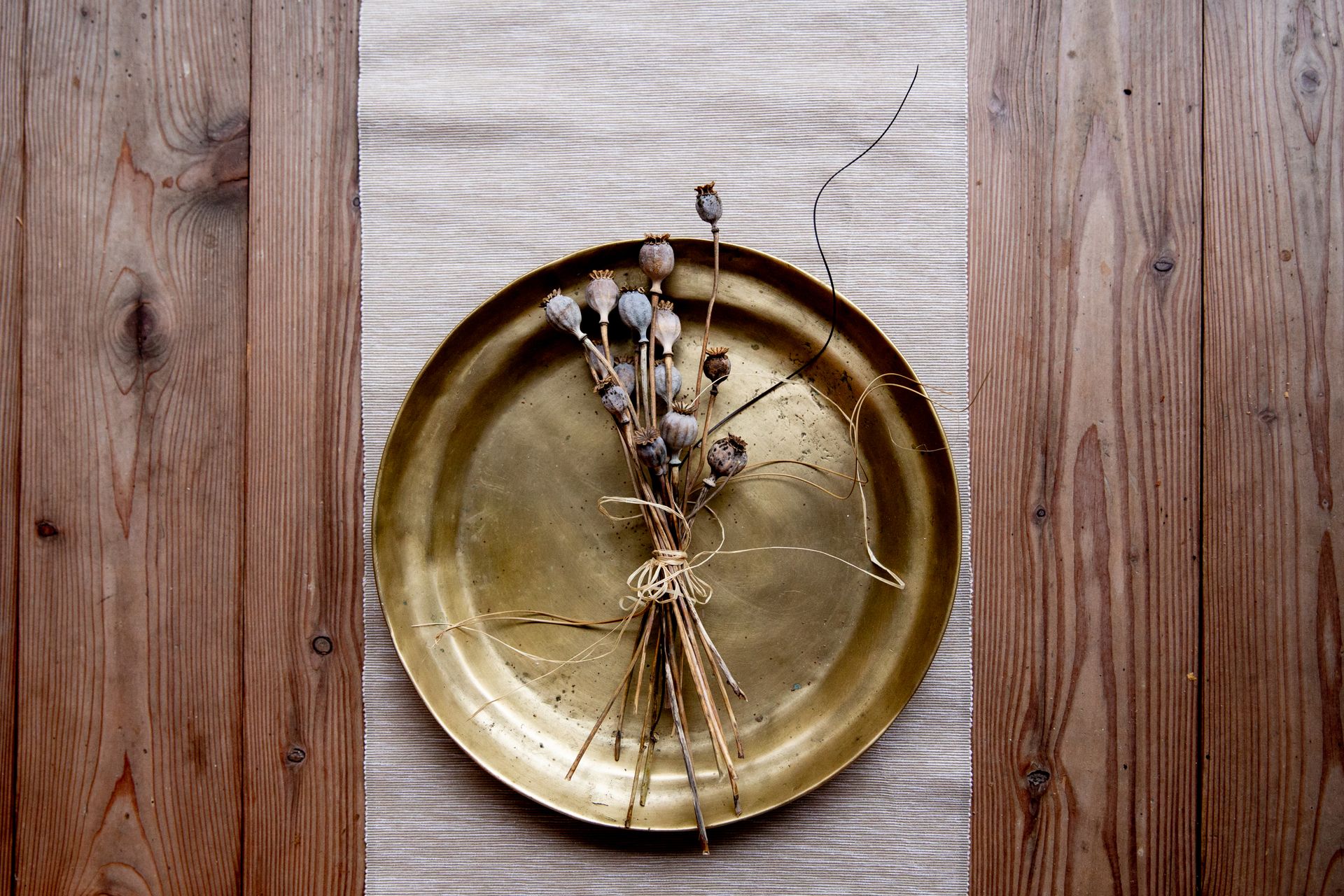 A vintage brass plate holds a bundle of dried flowers on a wooden table, creating a rustic aesthetic.