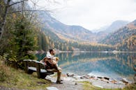 秋天，一位父亲和孩子坐在湖边的长凳上，背景是山脉