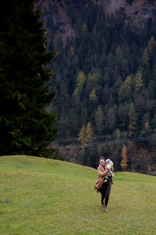 Woman in Brown Jacket and Black Pants Running on Grass Field