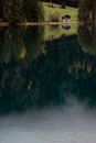 Picturesque view of calm lake reflecting amazing scenery of lonely country house on shore and forest in daytime