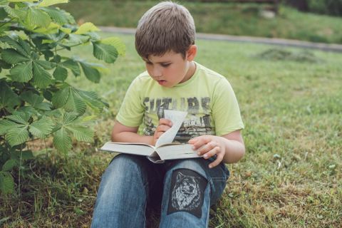 Boy reading a book outdoors — photo by Tanya Gorelova on Pexels