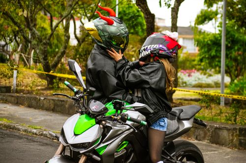 Free A couple wearing helmets embrace on a motorcycle in a park setting. Stock Photo
