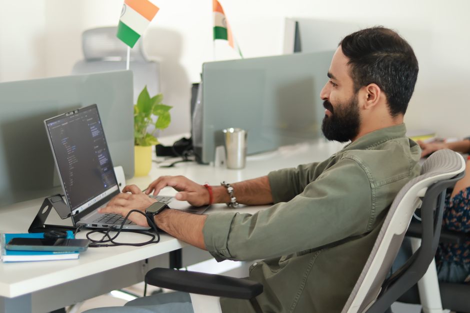 Young software developer typing code on a laptop in a modern office setting, focused on programming.