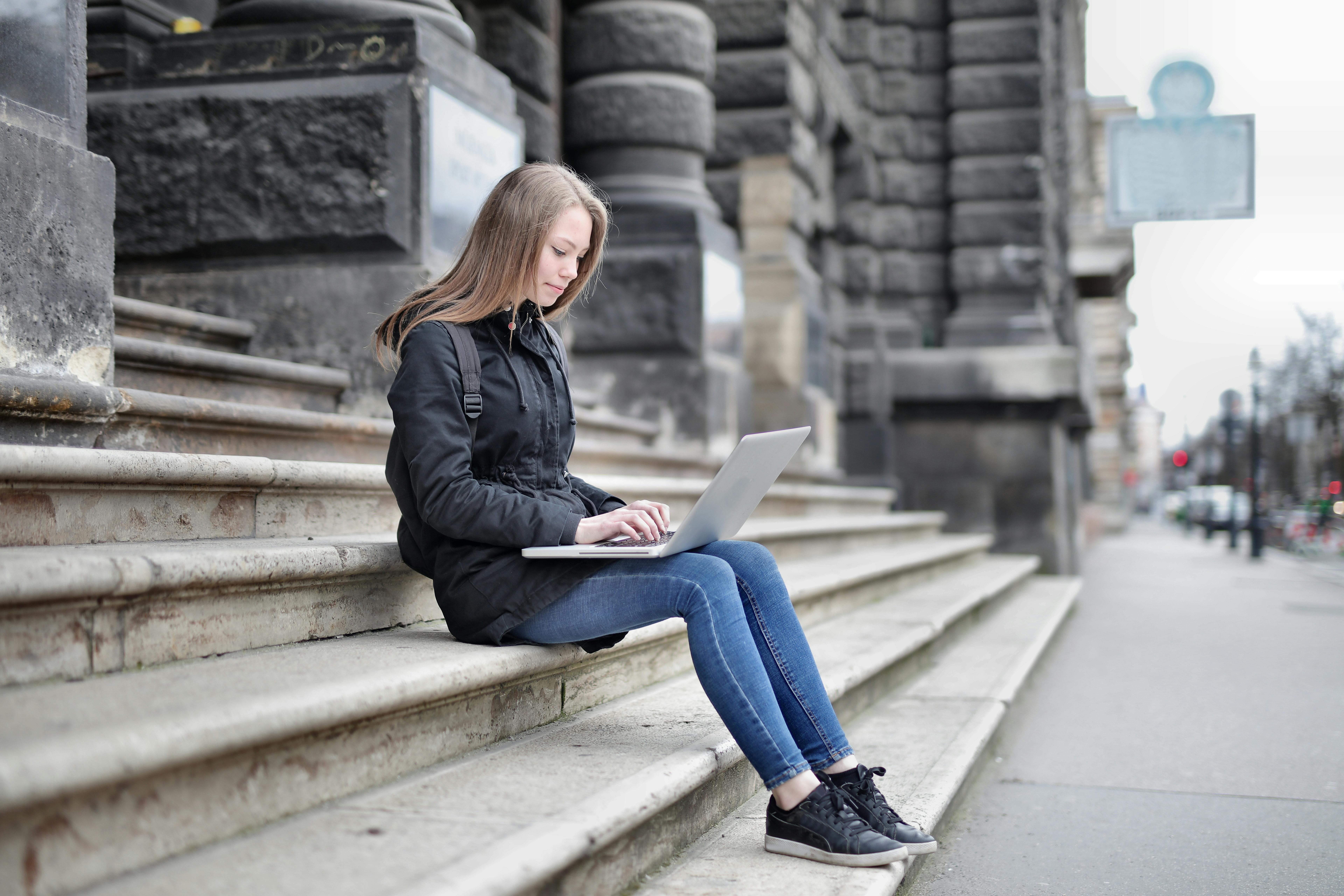 Woman using laptop seated on historic building steps for remote work.