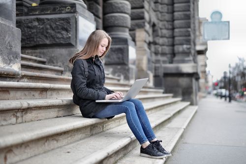 Free Woman using laptop seated on historic building steps for remote work. Stock Photo