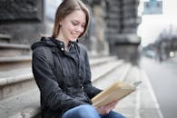 Woman in Black Jacket and Blue Denim Jeans Sitting on Concrete Stairs Reading Book