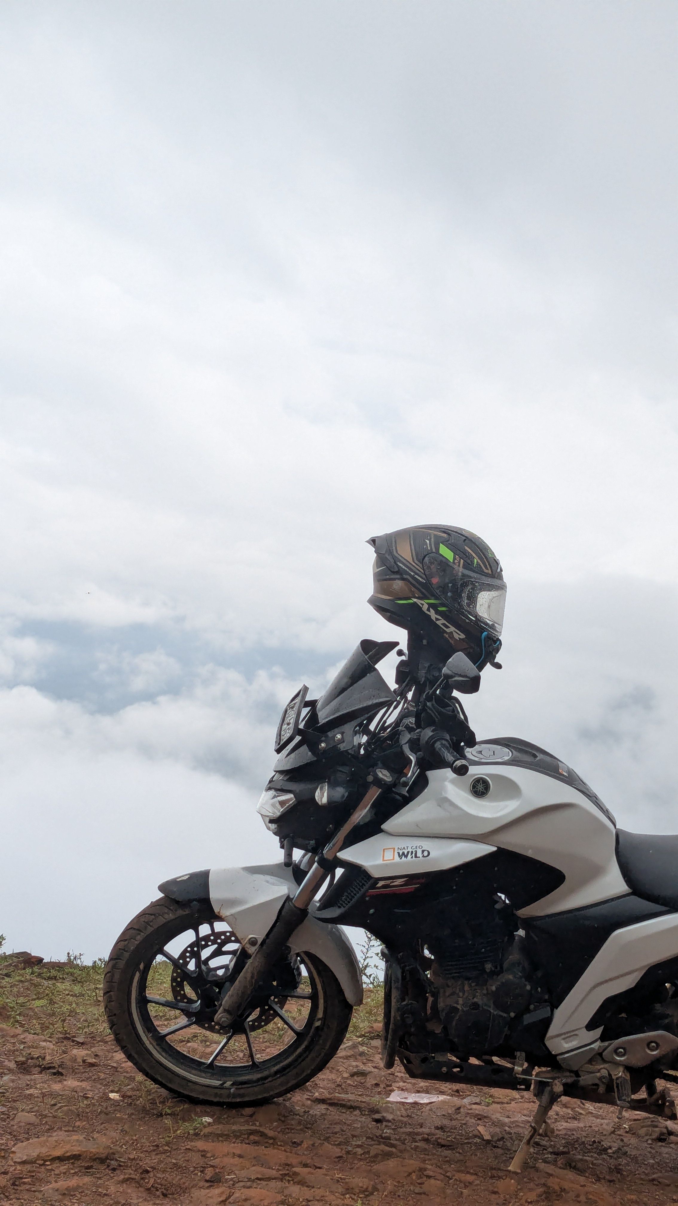 Motorcycle parked on a mountain with clouds in the background, evoking a sense of adventure.