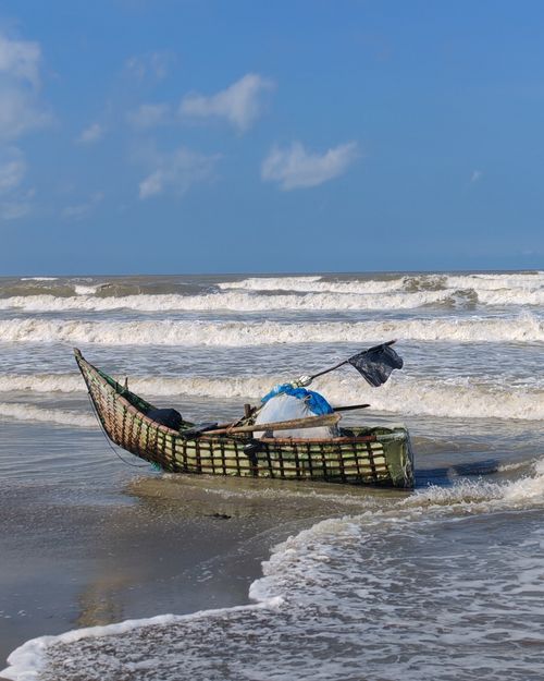 Free A traditional fishing boat rests on a sunny beach with waves crashing softly. Stock Photo