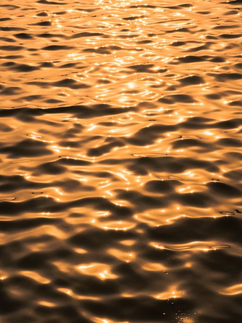 Free Rippling water reflecting golden hues of a sunset, creating a serene and mesmerizing pattern. Stock Photo