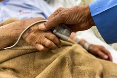 Crop old female patient lying on medical bed with pulse oximeter on finger and old man holding wrinkled hand