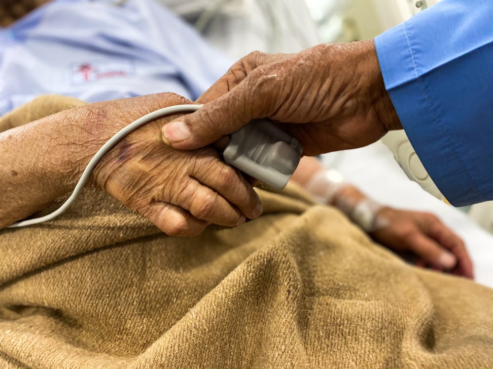 Crop old female patient lying on medical bed with pulse oximeter on finger and old man holding wrinkled hand