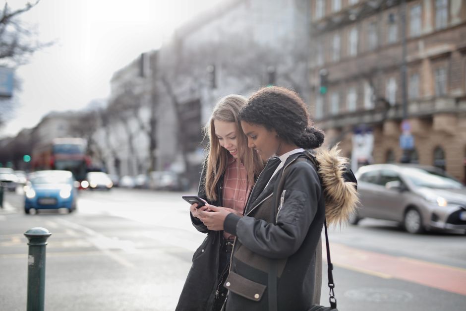 Two young women using a smartphone on a city street, enjoying the outdoor urban environment.
