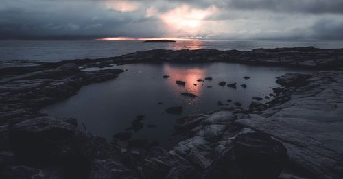 Free A breathtaking view of a rocky coastline during sunset with dramatic skies and reflections. Stock Photo
