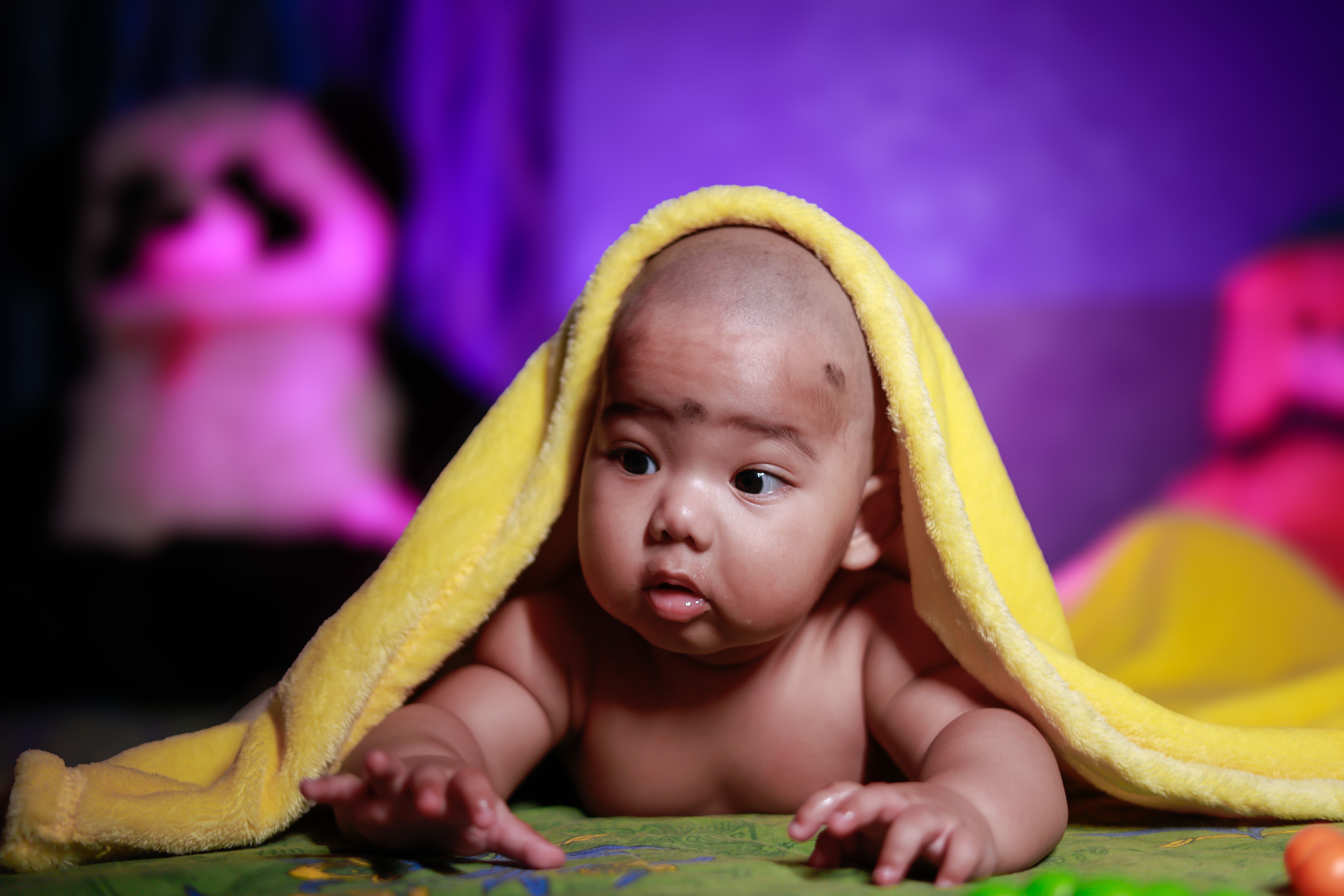 Cute baby under a yellow towel indoors, showcasing innocence and curiosity in a cozy setting.
