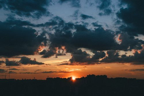 Free A dramatic sunset with silhouetted city skyline and vivid clouds. Stock Photo
