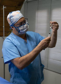 Doctor in protective clothing preparing a syringe for treatment in a hospital room.