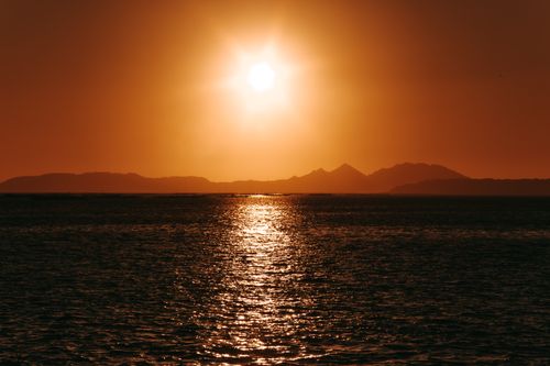 Free Peaceful sunset scene with glowing sun, tranquil ocean waters, and distant mountains. Stock Photo