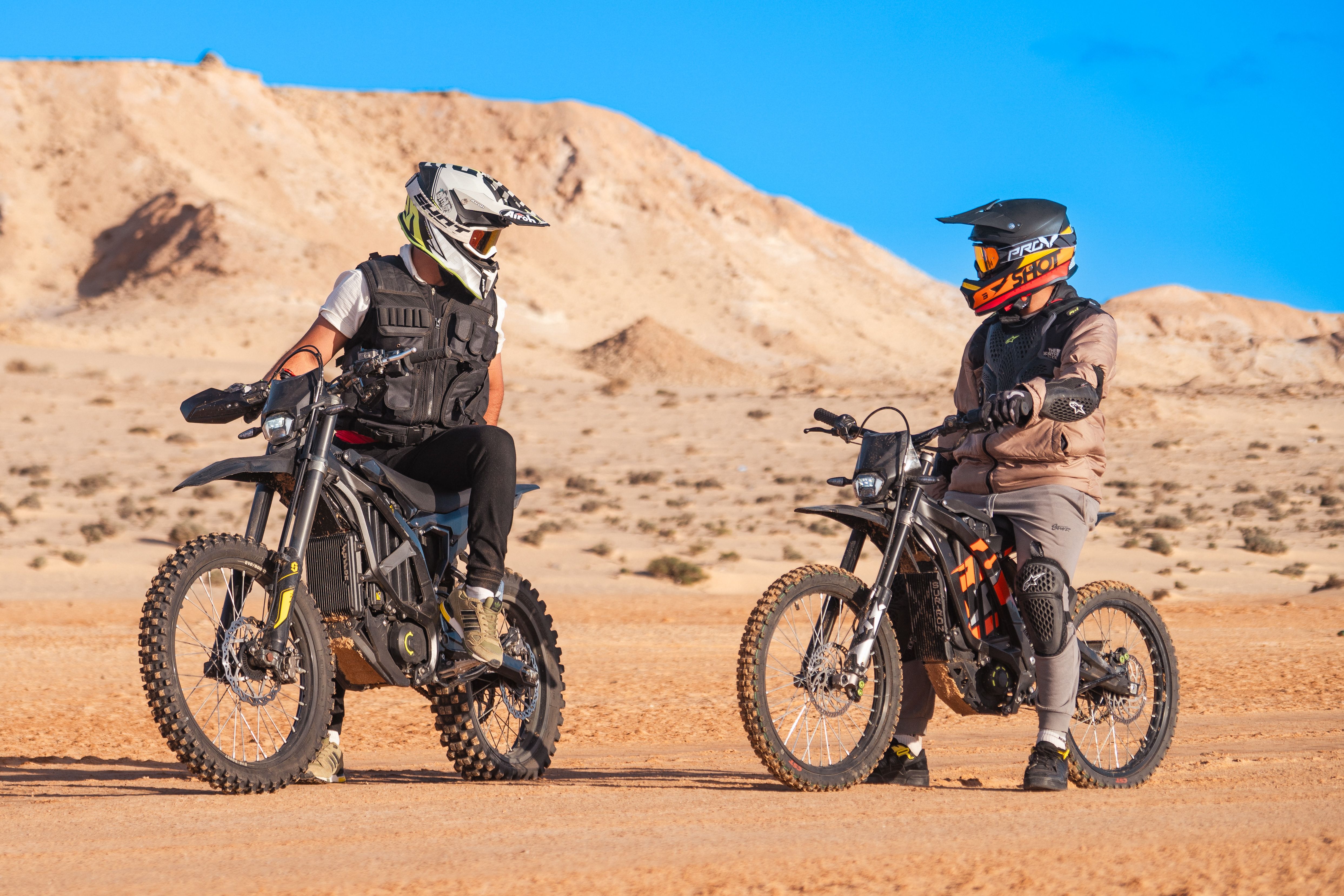 Two riders on electric bikes crossing a desert under a clear sky.