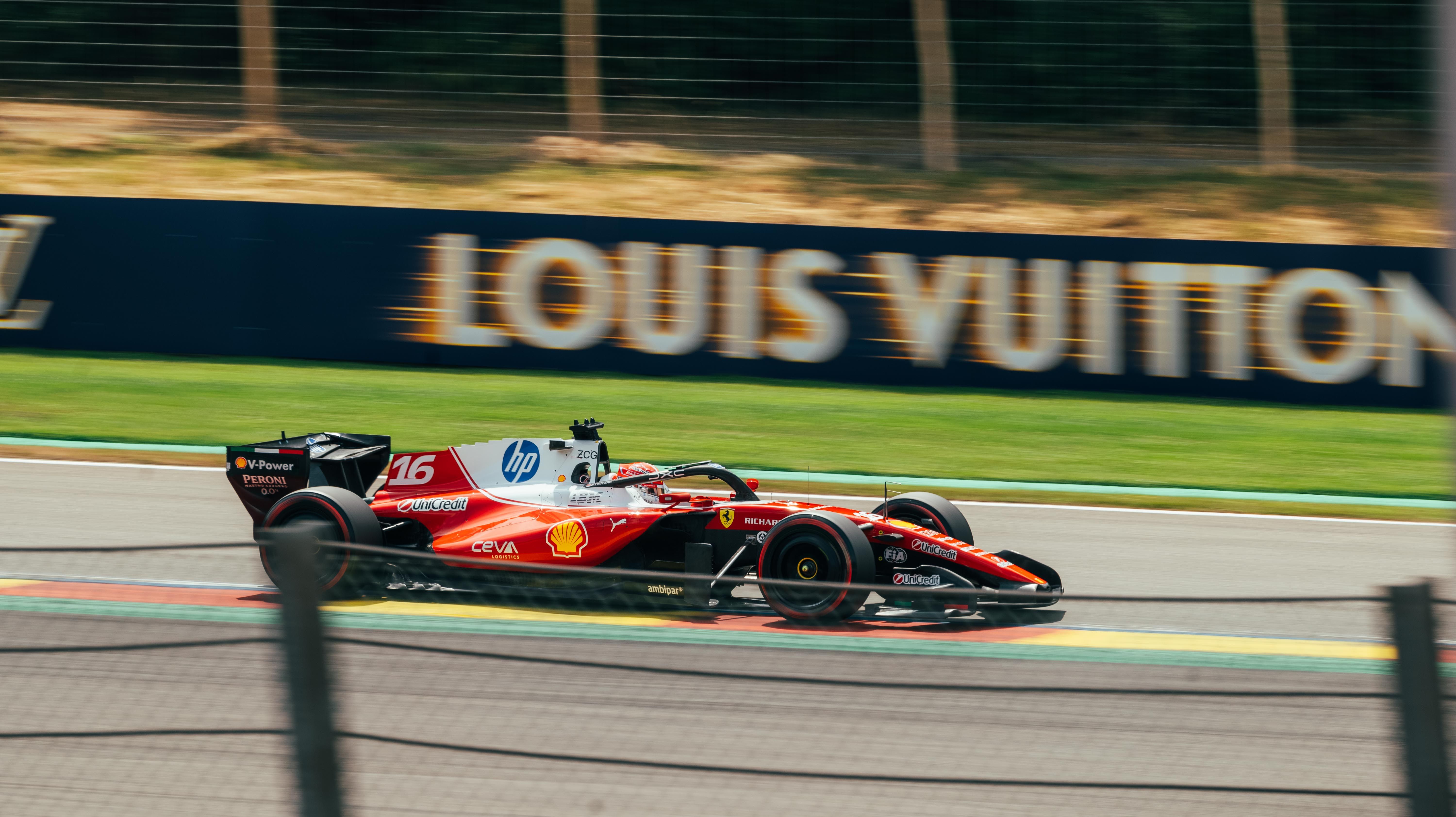 Red racing car speeds on track in Stavelot, Belgium at Spa-Francorchamps Circuit.