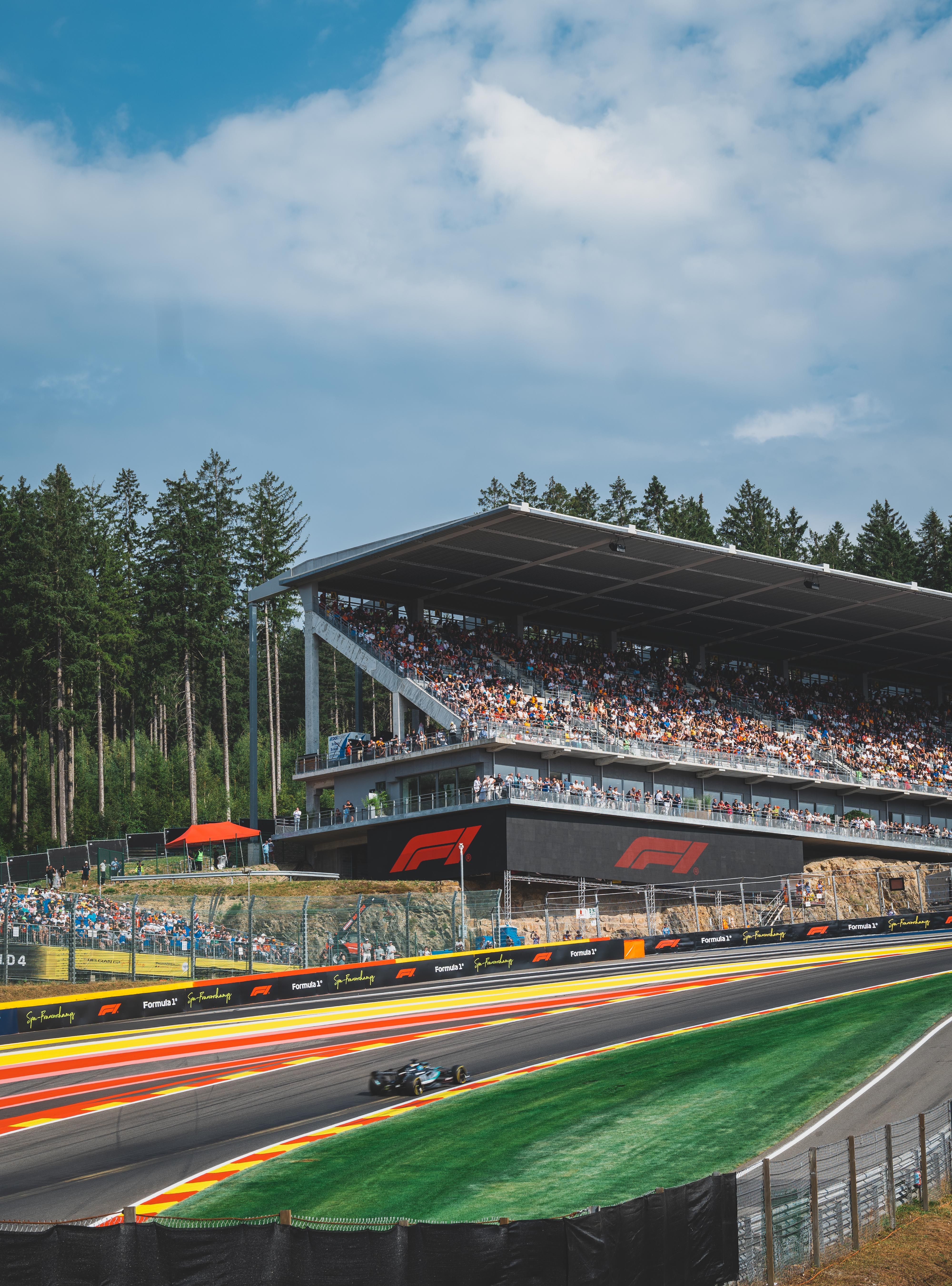 Een spannende Formule 1-race op het Circuit de Spa-Francorchamps in Stavelot, België, met een enthousiast publiek en een weelderig bos op de achtergrond.